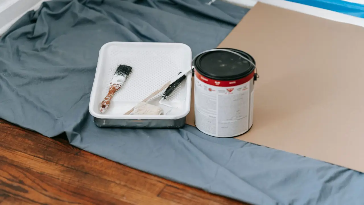 Bac, pinceau et pot de peinture poses sur une bache dans une piece en travaux
